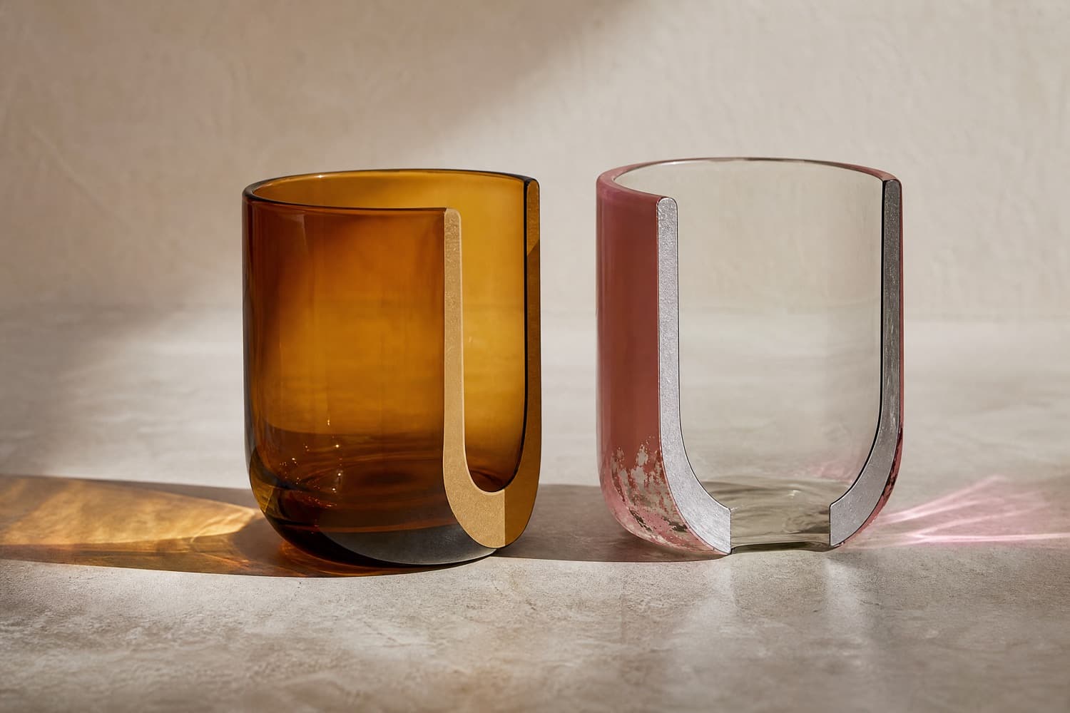 Two glass tumblers in cross-section: the left is amber through the full thickness of its wall, the right is clear glass with a thin pink surface layer that is visibly worn near the base.