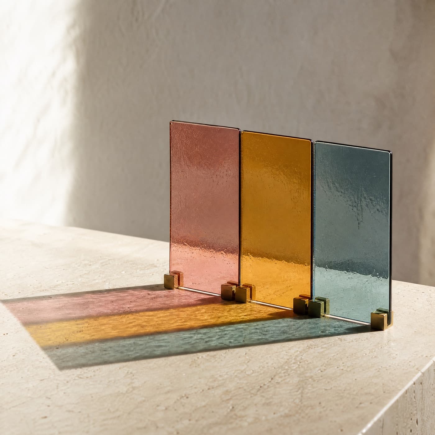 Three standing coloured glass panes on a sunlit sill, their projected rectangles overlapping into new colours.
