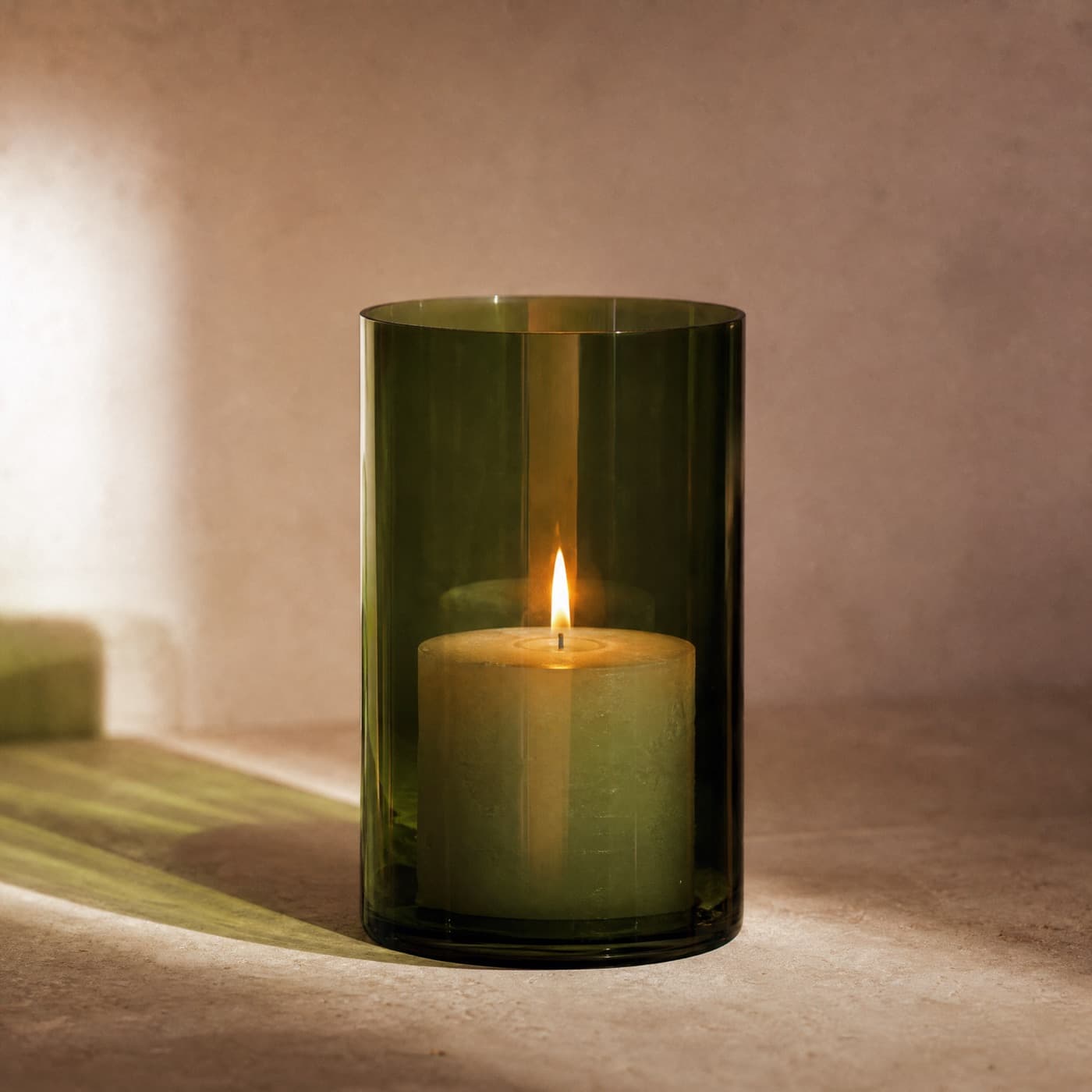 Glass-green hurricane lamp around a lit pillar candle, the shade glowing green in a dark room.