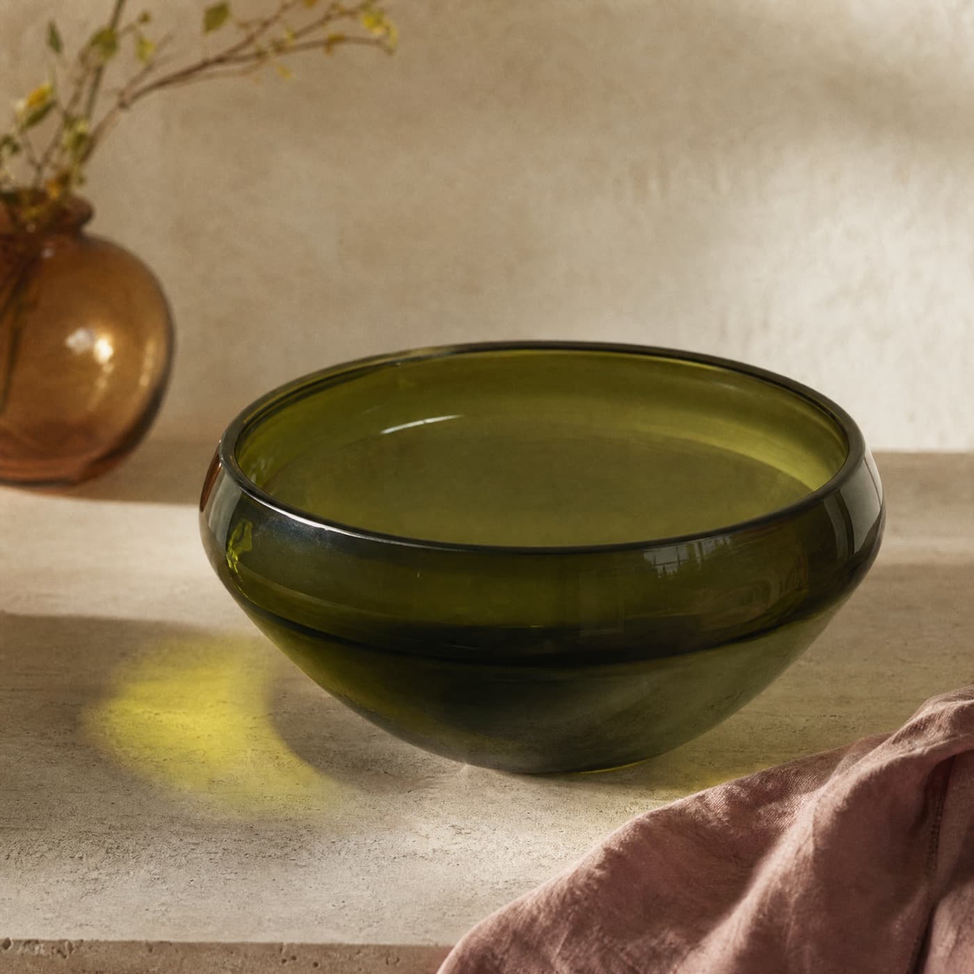 Large glass-green salad bowl on a table in daylight with a broad green shadow of colour beneath.