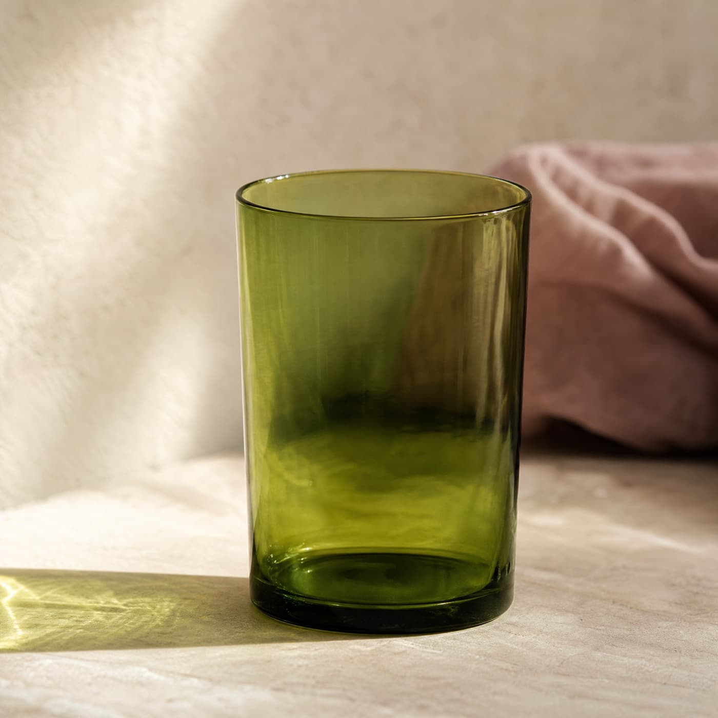 Tall glass-green water glass backlit, with a green colour patch falling across a pale table.