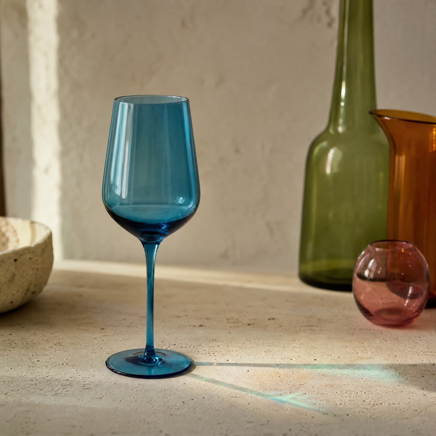 Sea-blue stemmed wine glass against a window, with a blue patch of light on the table beside its base.